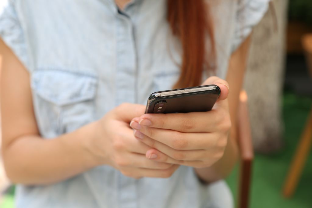 A ginger-haired woman checks her smartphone. Close-up of her hands holding the phone.