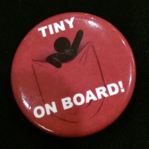 A small, red button with a tiny man in a pocket. The caption reads, "Tiny on board!"