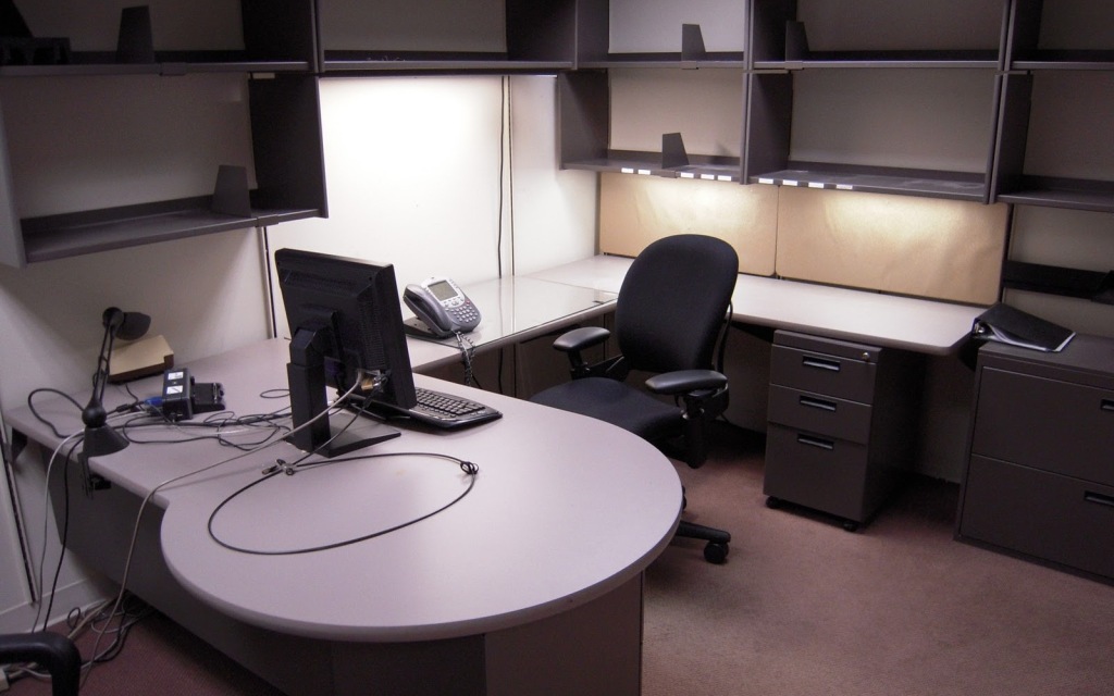 Empty corporate office, nothing on the shelves, monitor and keyboard sitting on bare desk.