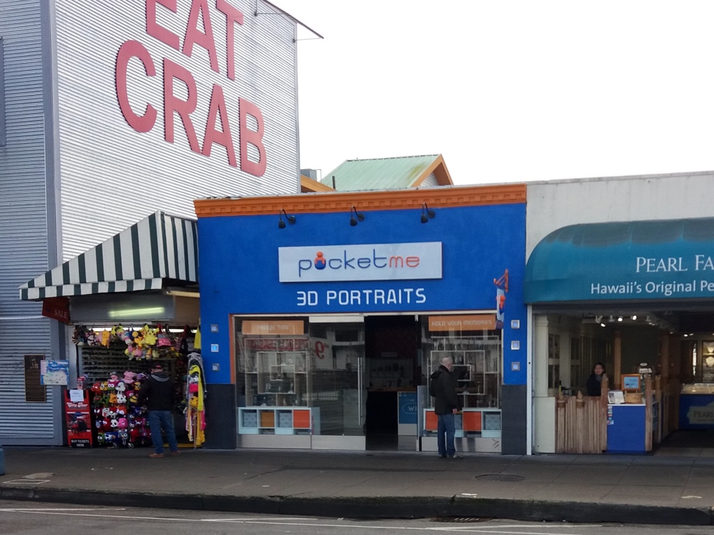 Under a gray, overcast California day, the bright blue PocketMe 3D Portraits store sits between a crab shack and a pearl market.