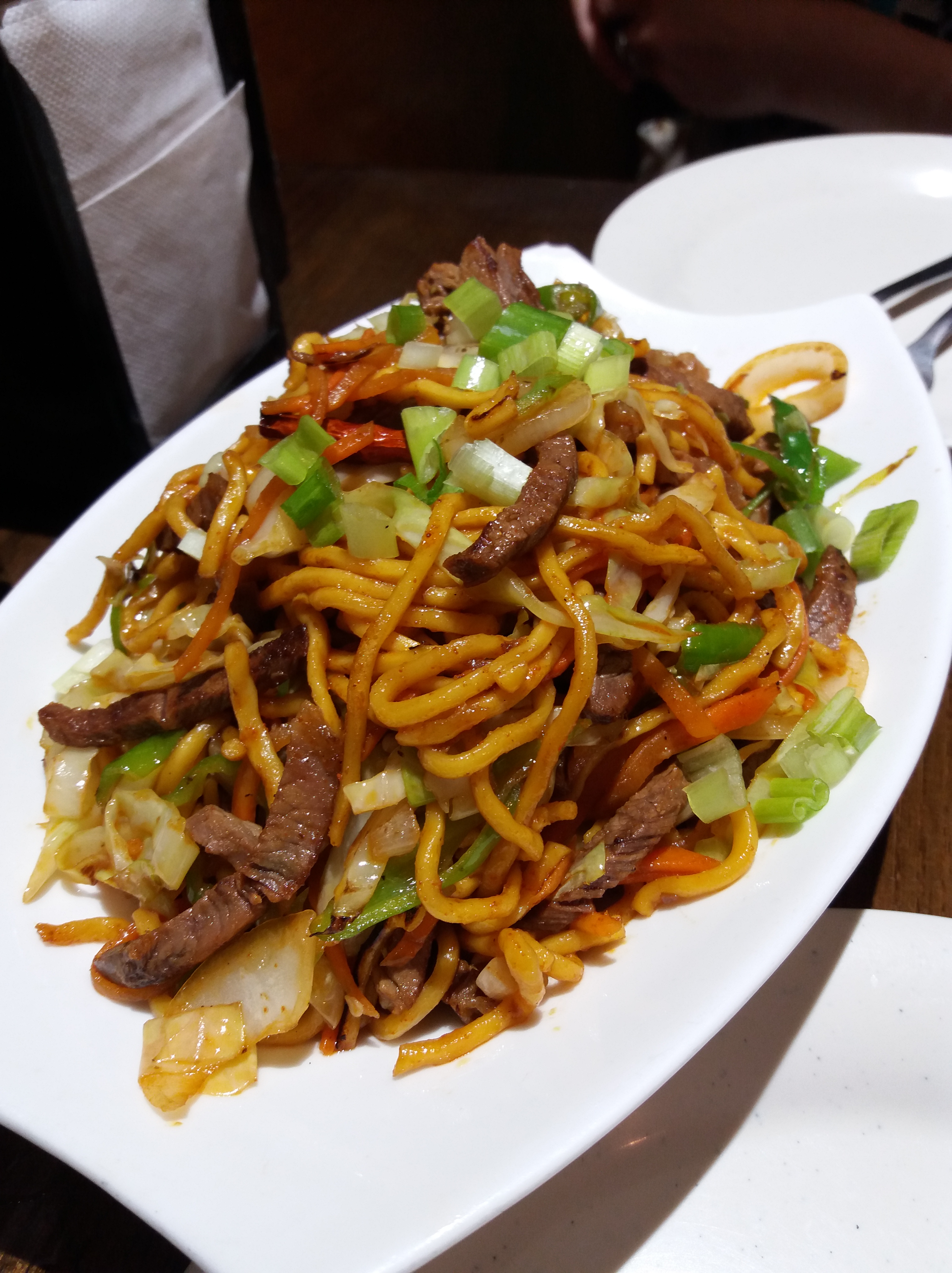 A big, overloaded plate of thick noodles and sliced, sauteed beef with vegetables.