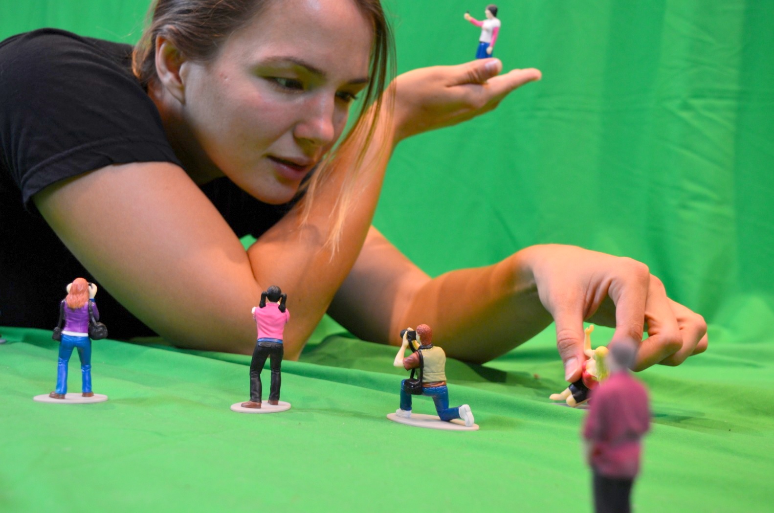 The model Koa leans over a selection of tiny people, interacting with their expressions.