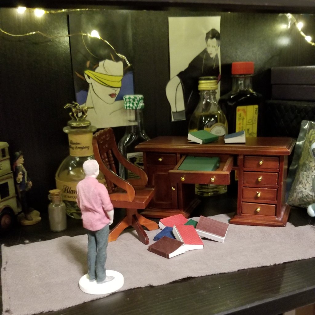 Tiny Aborigen stands before a miniature desk with a pile of books spilled around it.