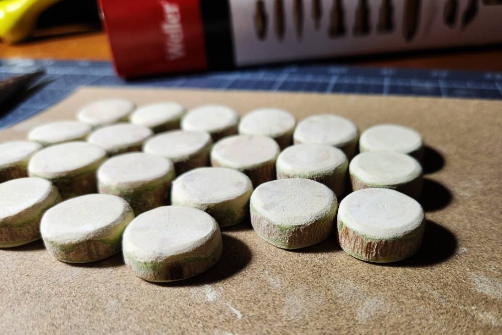 Four rows of small sanded disks with green bark on their perimeter, resting on sandpaper.